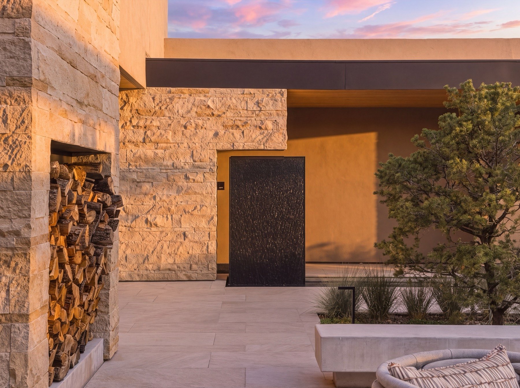 The entry courtyard at Resplendence at twilight, with a sculpted pine and a black water wall against glowing stone